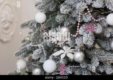 Nahaufnahme eines festlich geschmückten Weihnachtsbaums im Freien mit weißen und roten Kugeln auf verschwommenem glitzernden Feenhintergrund. Defokussed Girlande Lichter. Stockfoto