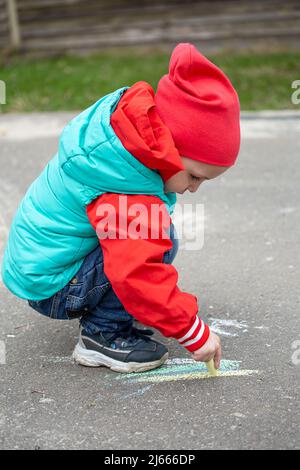 Ein kleines Mädchen zeichnet mit Kreide auf den Asphalt Stockfoto