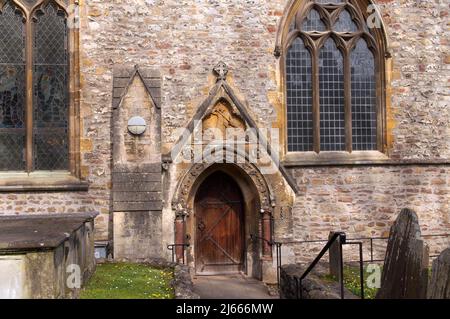 Alte hölzerne Seitentür an der Llandaff Kathedrale, die St. George zeigt, wie er den Drachen über dem Torbogen schlagt. Grabsteine und Gräber. Stockfoto