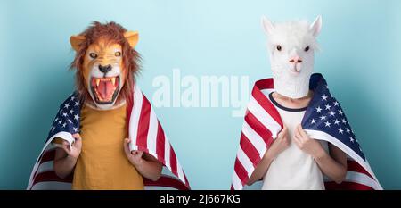 Junge Frau in Löwe und Alpaka-Maske halten USA US-amerikanische Flagge um die Schultern gewickelt, isoliert auf blauem Hintergrund Stockfoto