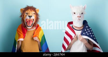 Eine junge Frau in einer Löwenmaske hält eine lgbt-Stolzflagge in Regenbogenfarben um die Schultern gewickelt und eine andere in einer Alpaka-Maske mit US-Flagge auf den Schultern, isoliert auf b Stockfoto