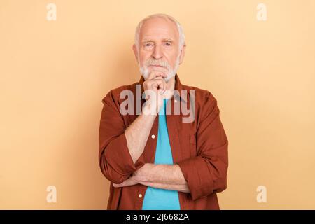 Foto von strengen Holder grau Frisur Mann denken tragen braunes Outfit isoliert auf beige Farbe Hintergrund Stockfoto