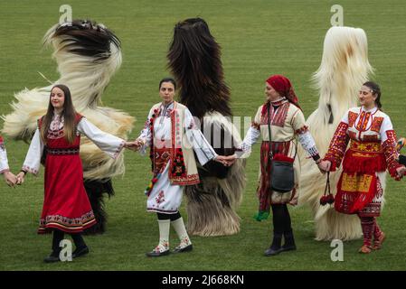 Bulgarische Mummers (Kukeri) und Frauen in traditionellen bulgarischen Kostümen tanzen im 'Simitli - antikes Land der Mummers' Stockfoto