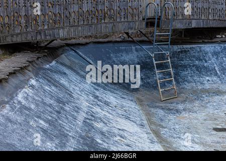 Der Raum eines leeren, alten Pools mit einer Treppe, die in ihn hinabsteigt. Hochwertige Fotos Stockfoto