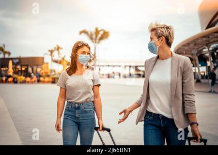 Reisende Frauen in Schutzmasken reden beim Verlassen des Flughafens am Zielort Stockfoto