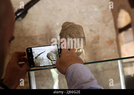 Ein palästinensischer Besucher fotografiert eine Steinstatue, die mit der kanaanitischen (Anah), der Göttin der Liebe und Schönheit, sowie der Göttin des Krieges, beschriftet ist, im 'Al-Basha' Palace Museum im Zentrum von Gaza City. Eine über 4.500 Jahre alte, neu entdeckte Steinstatuette, die das Gesicht einer alten Göttin nach Angaben des Ministerium für Altertümer und Tourismus in Gaza City darstellt. Die Steinstatue, die mit der kanaanäischen Göttin (Anah), der Göttin der Liebe und Schönheit sowie der Göttin des Krieges, beschriftet ist, Und ihr Charakter ist in der „mythologischen“ des kanaanäischen Glaubens prominent, sie wird die Jungfrau genannt, Stockfoto