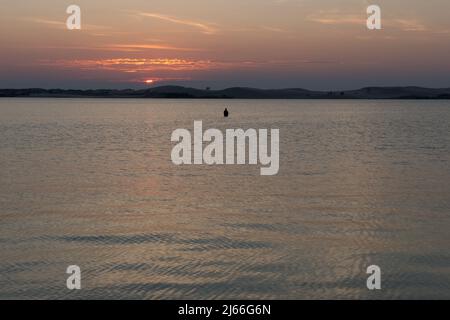 Ein einsitzender Fischer hütet sich tief im Wasser des Pentwater Lake bei Sonnenuntergang in Pentwater, Michigan, USA. Stockfoto