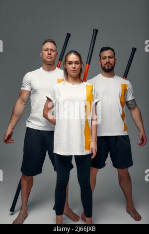 Menschen stehen zusammen und üben Stöcke. Karate-Meister posieren mit Stöcken im Studio zusammen. Stockfoto