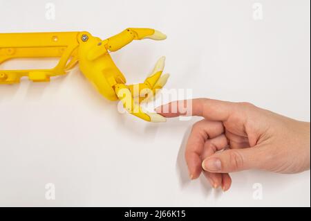 Frauenhand und eine Kunststoff-Handprothese für ein Kind auf weißem Hintergrund. Stockfoto