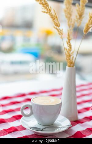 Eine Tasse Cappuccino steht in einem Café in einem hellen Innenraum auf dem Tisch Stockfoto