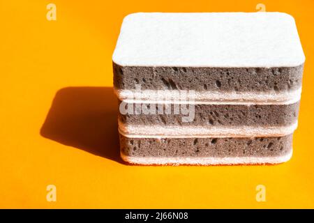 Drei graue Küchenschwämme auf dem orangen Hintergrund Stockfoto