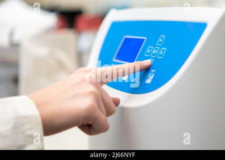 Frau stellt Parameter auf der Zentrifuge für die Probenvorbereitung ein. DNA, onkologische Markeranalyse im klinischen Labor. Stockfoto