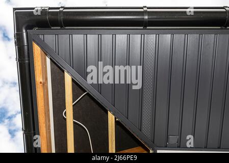 Gerüst mit drei Reihen von Holzlatten und einem modernen Graphitsoffit, sichtbaren H- und J-Lamellen und versteckter Steckdose. Stockfoto