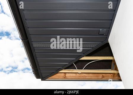 Gerüst mit drei Reihen von Holzlatten und einem modernen Graphitsoffit, sichtbaren H- und J-Lamellen und versteckter Steckdose. Stockfoto