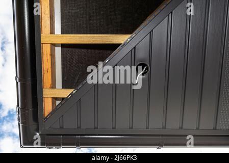 Gerüst mit drei Reihen von Holzlatten und einem modernen Graphitsoffit aus halbierten, sichtbaren H- und J-Lamellen. Stockfoto