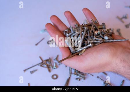 Mann Hand hält Stapel von rostigen Nägeln und Nüssen, sitzende Ansicht, oxidierte Nagel und Mutter auf dem Boden verstreut Stockfoto