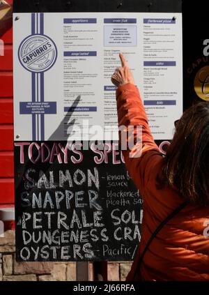 Ein Tourist schaut sich die Tafel-Speisekarte an, die Tagesgerichte in einem Fischrestaurant im Fisherman's Wharf-Viertel von San Francisco, Kalifornien, zeigt. Stockfoto