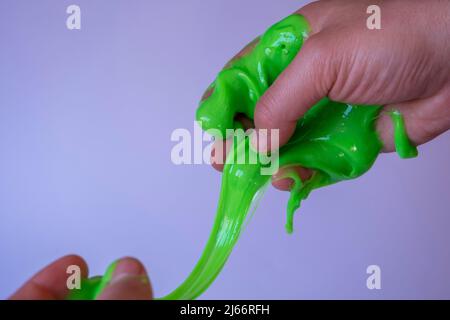 Grünes Schleim-Spielzeug auf Menschenhand, kämpfen und spielen mit Glitter grüner Schleim, isoliert auf weißem Hintergrund, Vorderansicht, Spielzeugkonzept Stockfoto