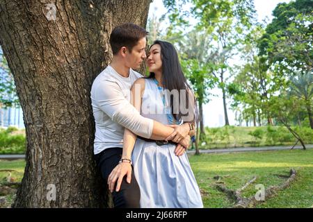 Multirassisches Paar, das kurz davor steht, sich an einen Baum zu lehnen Stockfoto