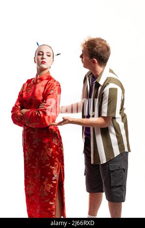 Multiethnisches Paar, männlich und weiblich. Frau in traditioneller roter chinesischer Tracht, die über ihre Schulter schaut, und Mann in Hemdfalte gekleidet und Stockfoto