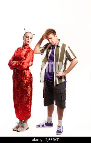 Multiethnisches Paar, männlich und weiblich. Frau in traditionellem chinesischen roten Kleid mit Blick über ihre Schulter und Mann in Hemd gekleidet denkend kratz Stockfoto
