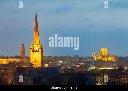 In Norwich, Norfolk, England, fällt die Nacht. Norwich Cathedral Turm im Vordergrund. Stockfoto