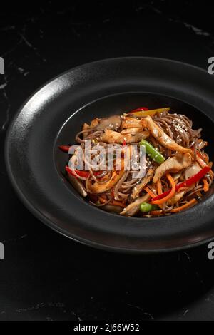 Draufsicht, Soba Chicken und Gemüse, Buchweizen-Nudeln auf dunklem Steingrund. Asiatische Küche, Wok-Menü. Traditionelle asiatische Küche, Wok-Menü. Vertic Stockfoto