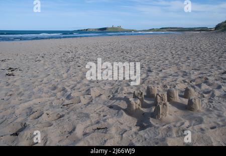 Breiter und offener Strand ohne Menschen mit einer kleinen Sandburg im Vordergrund und einem weit entfernten Dunstanburgh Castle an seinem Abhang im frühen Frühjahr Stockfoto