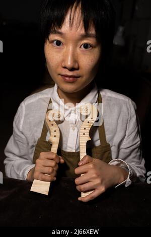 Die junge chinesische Geigenbauerin zeigt in ihrer Werkstatt den Hals der im Bau befindlichen Geigen Stockfoto