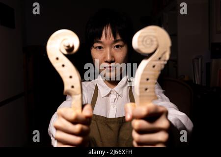 Die junge chinesische Geigenbauerin zeigt in ihrer Werkstatt den Hals der im Bau befindlichen Geigen Stockfoto