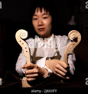 Die junge chinesische Geigenbauerin zeigt in ihrer Werkstatt den Hals der im Bau befindlichen Geigen Stockfoto