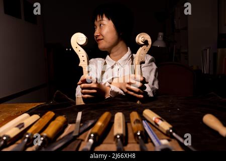 Die junge chinesische Geigenbauerin zeigt in ihrer Werkstatt den Hals der im Bau befindlichen Geigen Stockfoto