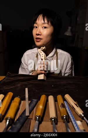 Die junge chinesische Geigenbauerin zeigt in ihrer Werkstatt den Hals der im Bau befindlichen Geigen Stockfoto