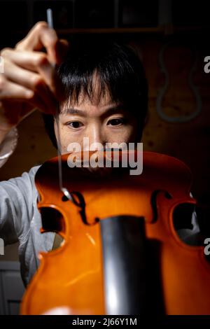 Die junge chinesische Geigenbauerin überprüft in der Werkstatt die Qualität ihrer Violine Stockfoto