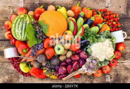 Eine Ernte von Obst, Gemüse und Beeren, gesammelt in einem großen Stapel auf einer hölzernen Arbeitsplatte. Stockfoto