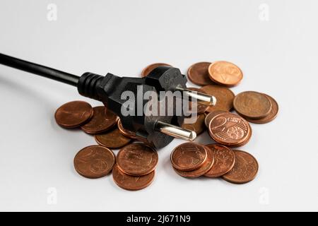 Schwarzer Stecker auf Münzen und weißem Hintergrund, Kosten für Strom und teures Energiekonzept Stockfoto