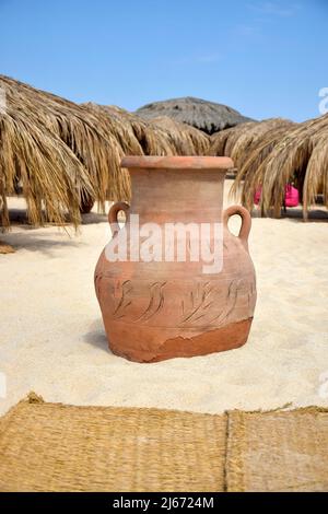 Lehmurne am Strand, vor dem Hintergrund von Sonnenschirmen, die an sonnigen Tagen mit trockenen Palmenblättern bedeckt sind. Vertikales Foto. Nahaufnahme. Selektiver Fokus. Stockfoto