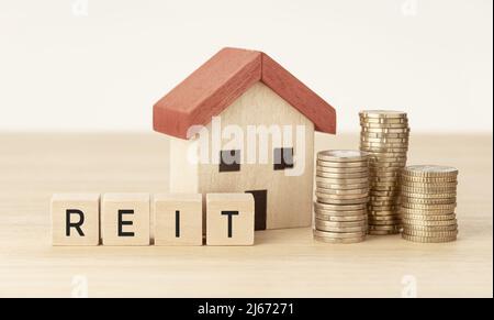 REIT Real Estate Investment Trust Konzept. Hausmodell, Geld und Holzblöcke mit Text Stockfoto