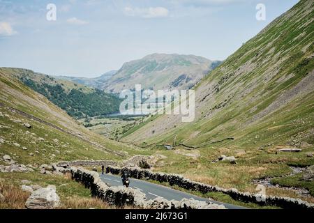 Ein Motorradfahrer, der auf dem Kirkstone Pass, Cumbria, fährt, und ein Radfahrer, der den Pass mit Blick auf einen kleinen tarn in der Ferne erkämpft Stockfoto