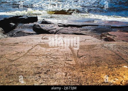 Alte Felszeichnungen am Ufer des Onega-Sees. Geschnitzt auf einer Granitplatte. Kap Besov Nos, Karelien, Russland - 15. August 2021. Stockfoto