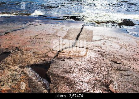 Alte Felszeichnungen am Ufer des Onega-Sees. Geschnitzt auf einer Granitplatte. Kap Besov Nos, Karelien, Russland - 15. August 2021. Stockfoto