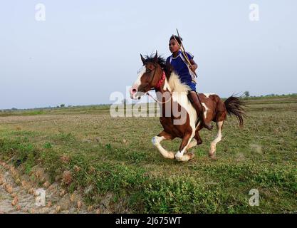 Ein junger Jockey reitet auf einem Pferd während eines Rural Horse Race. Nach der Erntezeit werden jedes Jahr in diesen Feldern Pferderennen veranstaltet. Die Jockeys, die Kinder sind, reiten Pferde ohne jegliche Schutz- oder Sicherheitsausrüstung. Stockfoto