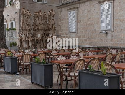 Außenbereich mit Tischen und Stühlen und großem Sonnenschirm, die befestigt sind und zusammen stehen Stockfoto