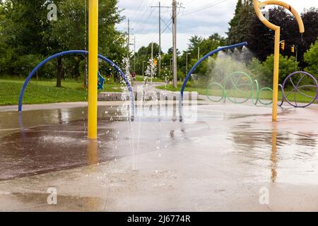 Spielplatz im öffentlichen Park im Sommer ohne Menschen. Springbrunnen mit Spritzwasser an einem sonnigen Tag. Stockfoto