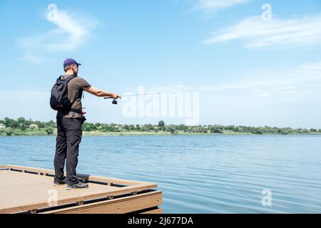 Fischer mit Spinnrute auf dem See. Fischer mit Spinning in den Händen fangen Fische an Sonnentag. Fischer mit Rute, Spinnrolle auf dem Fluss Stockfoto