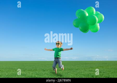 Glückliches Kind spielt mit hellen bunten Luftballons im Freien. Kind Spaß im grünen Frühlingsfeld vor blauem Himmel Hintergrund. Gesundes und aktives Leben Stockfoto