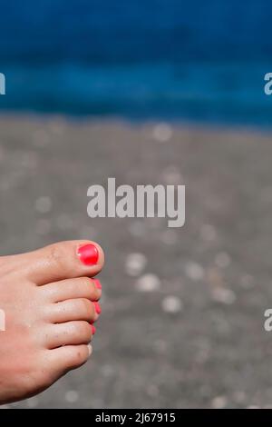 Nahaufnahme eines weiblichen Fußes mit rotem Nagellack zum Entspannen am Strand Stockfoto