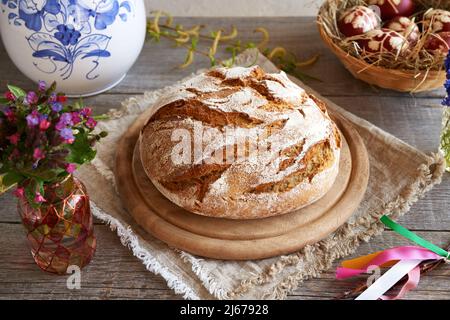 Ein Laib Sauerteig mit Ostereiern und Frühlingsblumen im Hintergrund Stockfoto