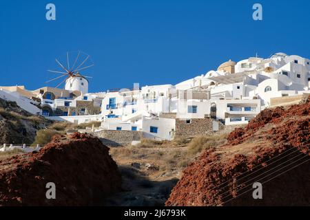 Eine weiß getünchte Windmühle und Hotels mit Balkonen auf der Spitze der vulkanischen Landschaft in Oia Santorini Stockfoto