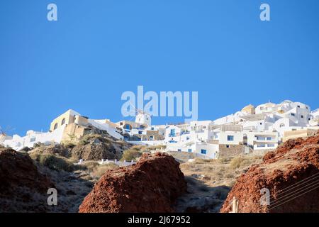 Eine weiß getünchte Windmühle und Hotels mit Balkonen auf der Spitze der vulkanischen Landschaft in Oia Santorini Stockfoto